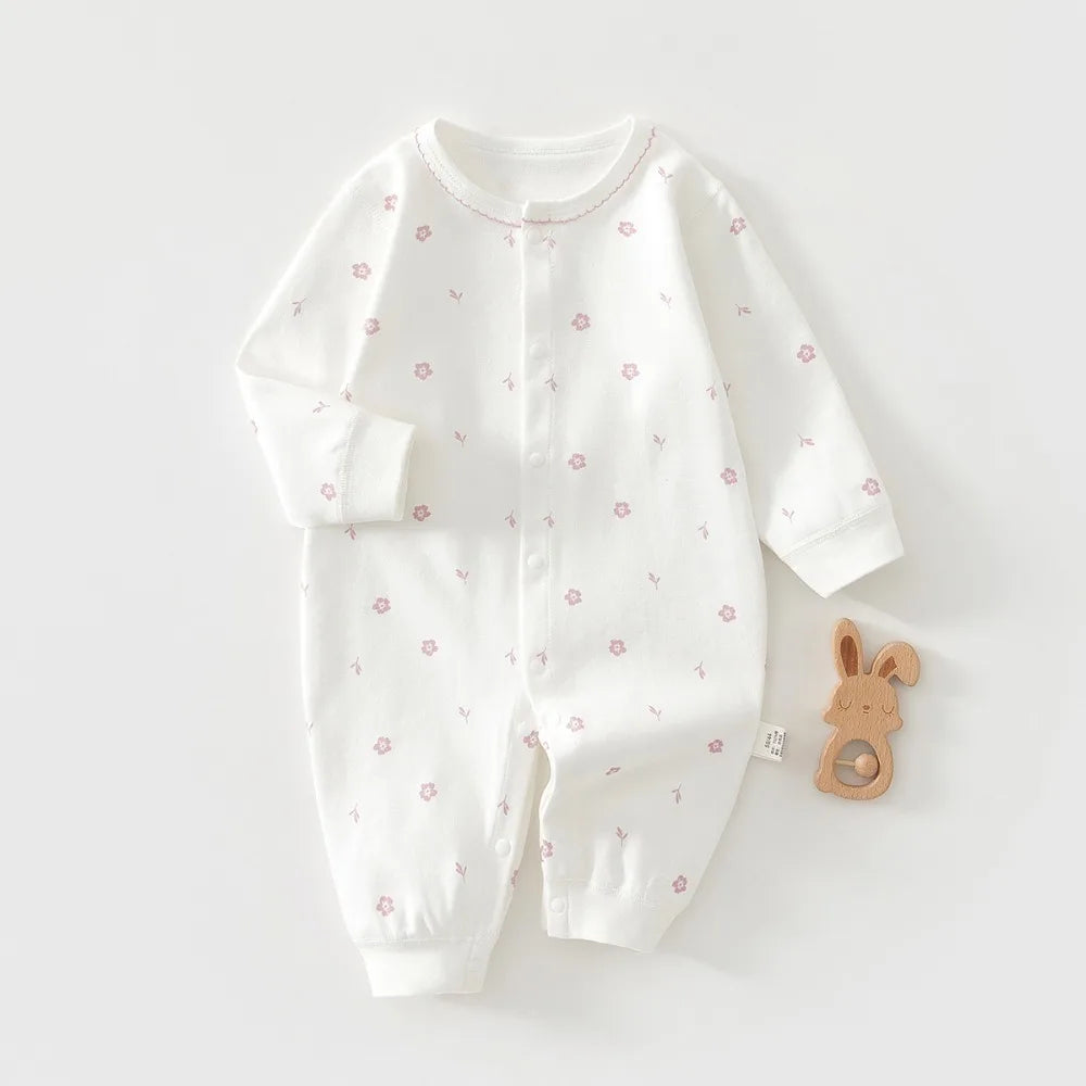 White baby onesie with pink floral patterns on a white background, accompanied by a wooden toy.