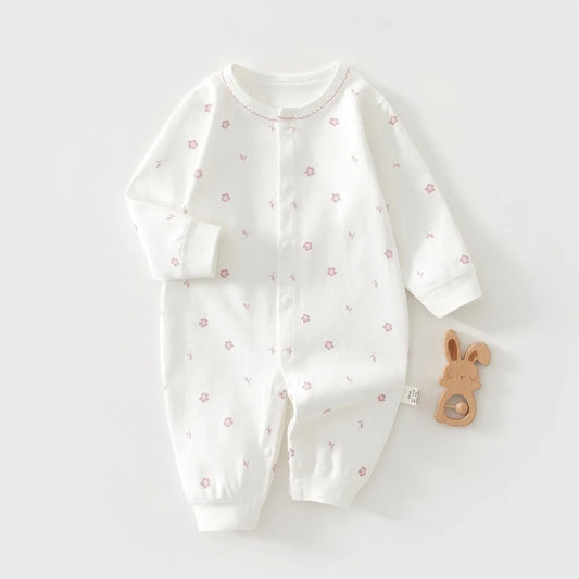 White baby onesie with pink floral patterns on a white background, accompanied by a wooden toy.