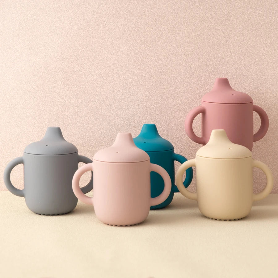 Set of colorful children's sippy cups on a beige background